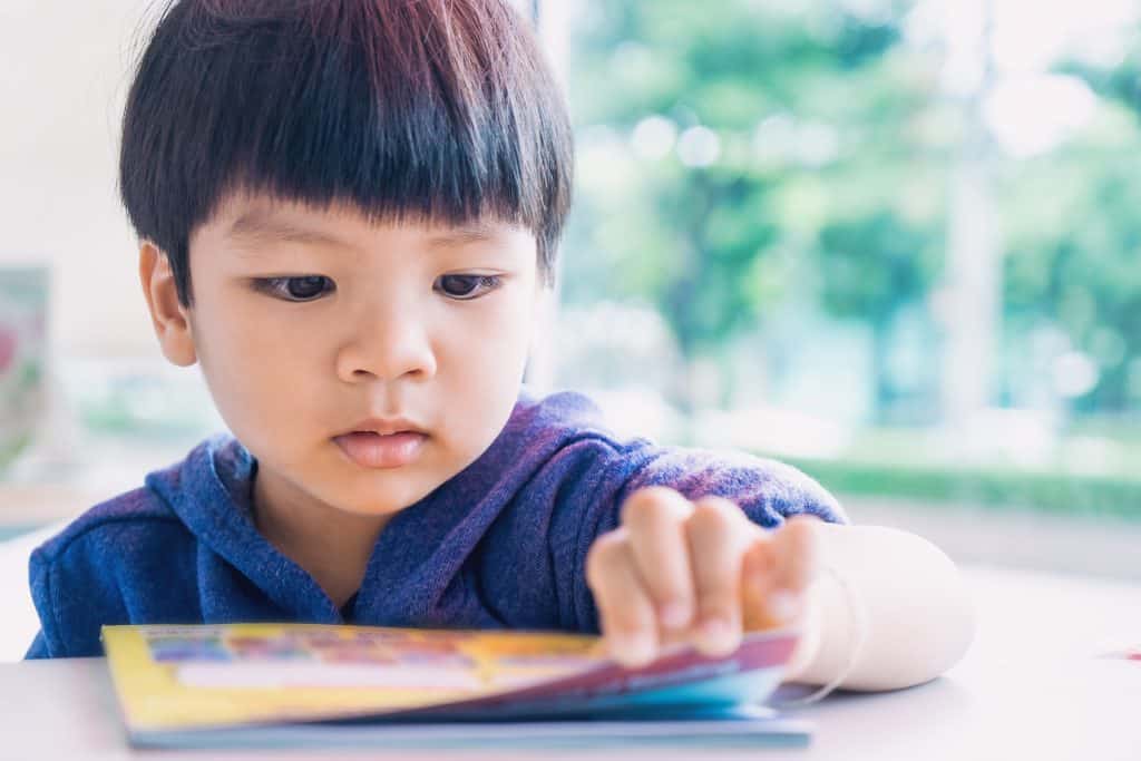 Young Asian-American boy reading a educational play book.